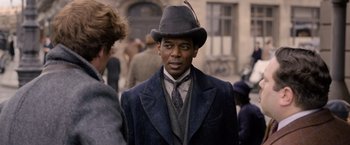 Movie still from “Fantastic Beasts: The Crimes of Grindelwald” (2018), directed by David Yates – A man wearing a suit and hat in a crowd of people; Close Up shot, Over the shoulder angle