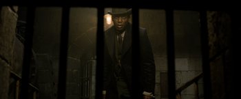 Movie still from “Fantastic Beasts: The Crimes of Grindelwald” (2018), directed by David Yates – A man in a suit and hat standing in front of a window; Medium shot, Low angle