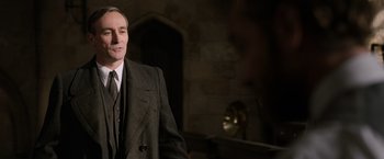 Movie still from “Fantastic Beasts: The Crimes of Grindelwald” (2018), directed by David Yates – A man wearing a suit and tie standing in a room; Close Up shot, Over the shoulder angle