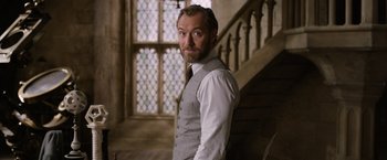 Movie still from “Fantastic Beasts: The Crimes of Grindelwald” (2018), directed by David Yates – A man standing in front of a staircase wearing a vest and tie; Medium shot, Low angle
