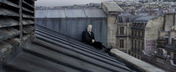 Movie still from “Fantastic Beasts: The Crimes of Grindelwald” (2018), directed by David Yates – A man sitting on the edge of a building; Wide shot, Low angle