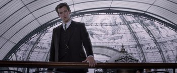 Movie still from “Fantastic Beasts: The Crimes of Grindelwald” (2018), directed by David Yates – A man in a suit and tie leaning on a railing; Medium shot, Low angle