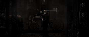 Movie still from “Fantastic Beasts: The Crimes of Grindelwald” (2018), directed by David Yates – A man standing in front of a horse drawn carriage; Wide shot, High angle