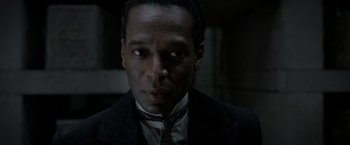 Movie still from “Fantastic Beasts: The Crimes of Grindelwald” (2018), directed by David Yates – A man wearing a suit and tie in a dark room; Close Up shot, Over the shoulder angle