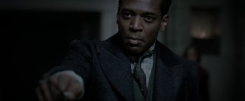 Movie still from “Fantastic Beasts: The Crimes of Grindelwald” (2018), directed by David Yates – A man wearing a suit and tie in a dark room; Close Up shot, Over the shoulder angle