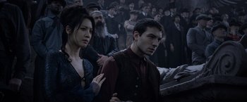 Movie still from “Fantastic Beasts: The Crimes of Grindelwald” (2018), directed by David Yates – A man and a woman standing next to each other in front of a group of people; Medium shot, Over the shoulder angle