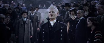 Movie still from “Fantastic Beasts: The Crimes of Grindelwald” (2018), directed by David Yates – A group of people standing around a man in a suit and tie; Medium shot, Low angle