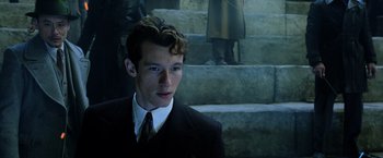 Movie still from “Fantastic Beasts: The Crimes of Grindelwald” (2018), directed by David Yates – A man in a suit and tie standing in front of some steps; Close Up shot, High angle