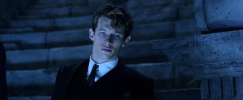 Movie still from “Fantastic Beasts: The Crimes of Grindelwald” (2018), directed by David Yates – A man in a suit and tie standing in front of some steps; Close Up shot, Low angle