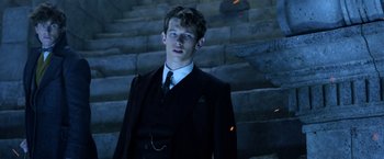 Movie still from “Fantastic Beasts: The Crimes of Grindelwald” (2018), directed by David Yates – A man in a suit and tie standing in front of some steps; Medium shot, Low angle