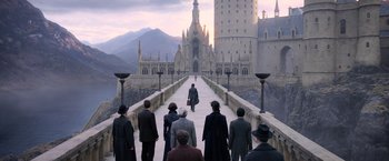 Movie still from “Fantastic Beasts: The Crimes of Grindelwald” (2018), directed by David Yates – A group of people standing on top of a bridge near a castle; Extreme Wide shot, High angle