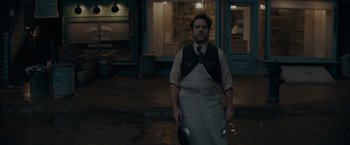 Movie still from “Fantastic Beasts: The Secrets of Dumbledore” (2022), directed by David Yates – A man standing on the sidewalk holding a frying pan; Medium shot, High angle