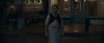 Movie still from “Fantastic Beasts: The Secrets of Dumbledore” (2022), directed by David Yates – A man standing on the sidewalk in front of a building; Medium shot, High angle