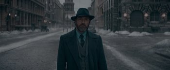 Movie still from “Fantastic Beasts: The Secrets of Dumbledore” (2022), directed by David Yates – A man wearing a suit and hat standing in the middle of the street; Medium shot, Low angle
