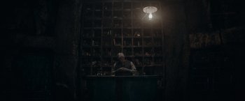 Movie still from “Fantastic Beasts: The Secrets of Dumbledore” (2022), directed by David Yates – An old man sitting at a table in front of shelves of books; Wide shot, High angle