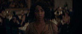 Movie still from “Fantastic Beasts: The Secrets of Dumbledore” (2022), directed by David Yates – A woman in a gold dress is standing in front of candles; Close Up shot, Over the shoulder angle