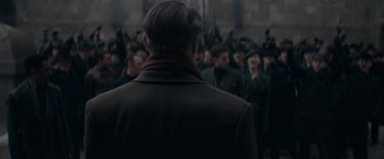 Movie still from “Fantastic Beasts: The Secrets of Dumbledore” (2022), directed by David Yates – A crowd of men in coats and hats standing in a crowd; Medium shot, Over the shoulder angle
