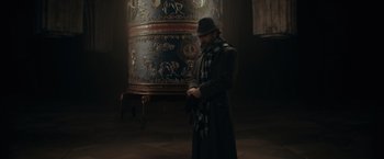 Movie still from “Fantastic Beasts: The Secrets of Dumbledore” (2022), directed by David Yates – A man in a long coat and a hat standing in front of a large vase; Wide shot, High angle