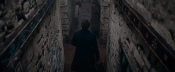 Movie still from “Fantastic Beasts: The Secrets of Dumbledore” (2022), directed by David Yates – A person walking down a dark hallway with a suitcase; Wide shot, High angle