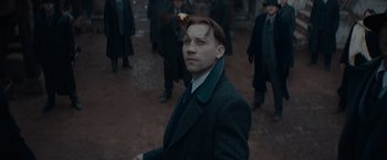 Movie still from “Fantastic Beasts: The Secrets of Dumbledore” (2022), directed by David Yates – A man in a suit and tie standing next to other men; Close Up shot, Low angle