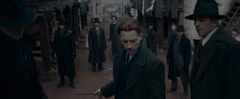 Movie still from “Fantastic Beasts: The Secrets of Dumbledore” (2022), directed by David Yates – A man in a suit and tie holding a wand in front of a group of people; Medium shot, Over the shoulder angle