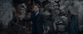 Movie still from “Fantastic Beasts: The Secrets of Dumbledore” (2022), directed by David Yates – A man in a suit standing in front of a flock of birds; Medium shot, Low angle