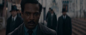 Movie still from “Fantastic Beasts: The Secrets of Dumbledore” (2022), directed by David Yates – A man in a suit and tie looking at the camera; Close Up shot, Over the shoulder angle