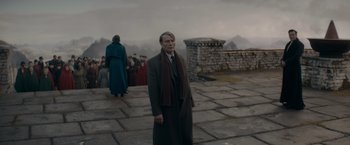 Movie still from “Fantastic Beasts: The Secrets of Dumbledore” (2022), directed by David Yates – A man standing on a stone walkway in front of a group of people; Wide shot, Low angle