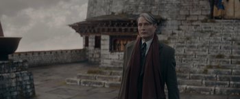 Movie still from “Fantastic Beasts: The Secrets of Dumbledore” (2022), directed by David Yates – A man wearing a suit and tie standing in front of a stone building; Medium shot, Low angle