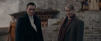 Movie still from “Fantastic Beasts: The Secrets of Dumbledore” (2022), directed by David Yates – Two men standing next to each other in front of a stone wall; Close Up shot, Low angle