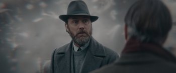 Movie still from “Fantastic Beasts: The Secrets of Dumbledore” (2022), directed by David Yates – A man wearing a hat and a gray coat; Close Up shot, Low angle