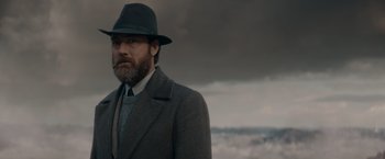 Movie still from “Fantastic Beasts: The Secrets of Dumbledore” (2022), directed by David Yates – A man with a beard wearing a hat and a suit; Medium shot, Low angle
