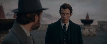Movie still from “Fantastic Beasts: The Secrets of Dumbledore” (2022), directed by David Yates – A man wearing a suit and tie standing next to another man wearing a hat; Close Up shot, Over the shoulder angle