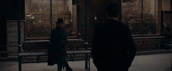 Movie still from “Fantastic Beasts: The Secrets of Dumbledore” (2022), directed by David Yates – A man sitting on top of a bench next to another man; Wide shot, Over the shoulder angle