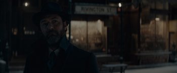 Movie still from “Fantastic Beasts: The Secrets of Dumbledore” (2022), directed by David Yates – A man wearing a hat and a suit standing in front of a street sign; Close Up shot, Over the shoulder angle