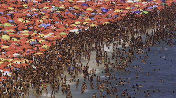 Movie still from “Fantastic Fungi” (2019), directed by Louie Schwartzberg – A crowd of people in the water at the beach; Extreme Wide shot, Overhead angle