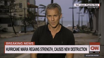 Movie still from “Fantastic Fungi” (2019), directed by Louie Schwartzberg – A man in a black shirt is standing in front of a building; Medium shot, Over the shoulder angle