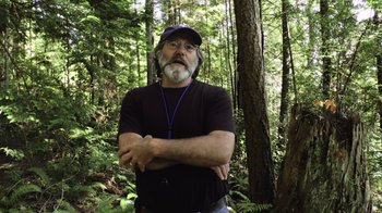 Movie still from “Fantastic Fungi” (2019), directed by Louie Schwartzberg – A man standing in the middle of a forest with his arms crossed; Medium shot, Low angle