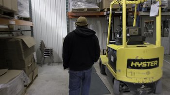 Movie still from “Fantastic Fungi” (2019), directed by Louie Schwartzberg – A man standing in front of a yellow forklift; Wide shot, Over the shoulder angle