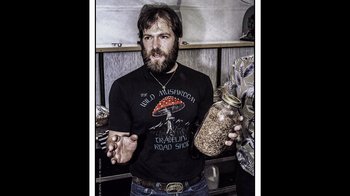 Movie still from “Fantastic Fungi” (2019), directed by Louie Schwartzberg – A bearded man holding a jar full of seeds; Medium shot, Overhead angle