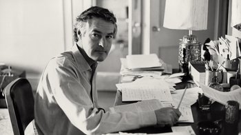 Movie still from “Fantastic Fungi” (2019), directed by Louie Schwartzberg – A black and white photo of a man sitting at a table with papers; Close Up shot, Low angle
