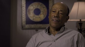 Movie still from “Fantastic Fungi” (2019), directed by Louie Schwartzberg – An older man sitting in front of a wall clock; Close Up shot, Low angle