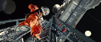 Movie still from “Ad Astra” (2019), directed by James Gray – A man in an orange suit standing on top of a metal fence; Wide shot, Overhead angle