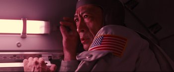 Movie still from “Ad Astra” (2019), directed by James Gray – A man in a white jacket with an american flag on it; Close Up shot, Low angle
