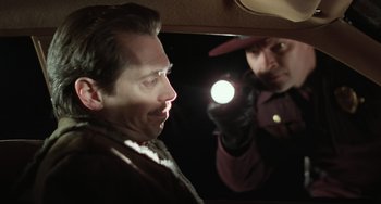 Movie still from “Fargo” (1996), directed by Ethan Coen – A man is looking at himself in the mirror while another man holds up a flashlight; Close Up shot, Over the shoulder angle