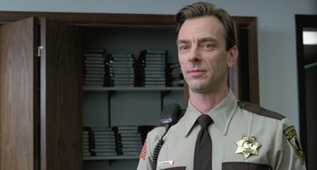 Movie still from “Fargo” (1996), directed by Ethan Coen – A man in a sheriff's uniform stands in front of a book case; Close Up shot, Low angle