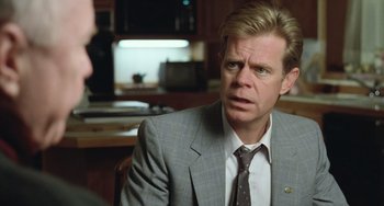 Movie still from “Fargo” (1996), directed by Ethan Coen – A man wearing a suit and tie sitting in front of a counter; Close Up shot, Over the shoulder angle
