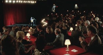 Movie still from “Fargo” (1996), directed by Ethan Coen – A group of people sitting at tables in front of a microphone; Extreme Wide shot, High angle