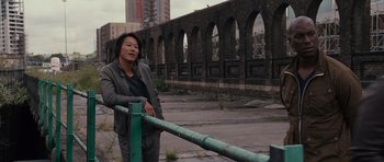 Movie still from “Fast & Furious 6” (2013), directed by Justin Lin – A person standing next to a green railing in an urban setting; Medium shot, Over the shoulder angle