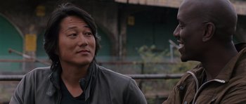 Movie still from “Fast & Furious 6” (2013), directed by Justin Lin – A man standing next to another man on a street; Close Up shot, Over the shoulder angle